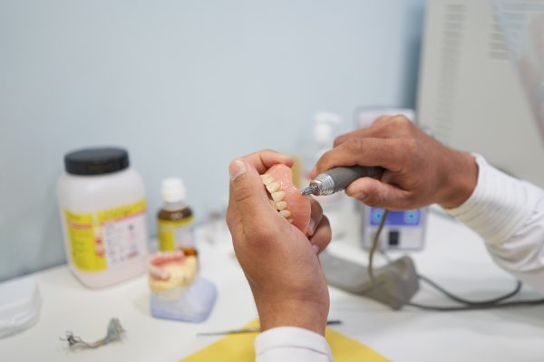 Male prosthetic, retouching a denture in the workshop. Concept, medicine and health